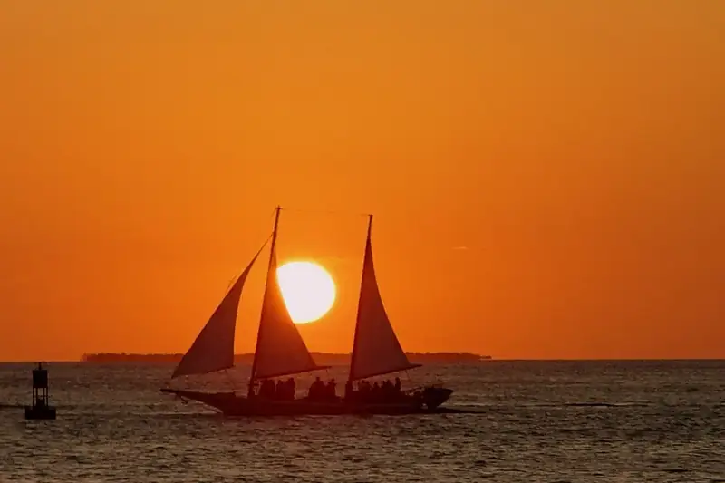 Velero de dos mástiles a contraluz con un atardecer naranja